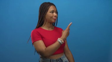 Mavi duvarlı ve örgülü saçları görünen bir stüdyoda sağı gösteren bir kadın. Düşünceli bir merak..