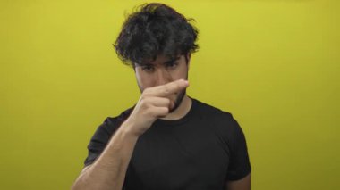 Sakallı bir adam sarı arka planda hareketler yapıyor, dikkati ve yoğunluğu vurguluyor, dikkat, odaklanma ve iletişim temaları için mükemmel..