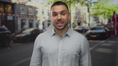 Genç İspanyol adam gülümsüyor ve iyi işaret veriyor. Meşgul caddede yükselen elle. İyimserlik, iyimserlik, iyimserlik, pozitif teşvik..