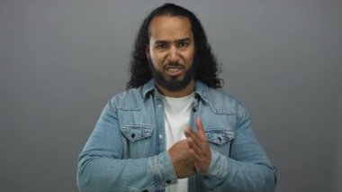 Erkek, gri stüdyoda, kot ceket ve beyaz tişört giyerek avuç içi ve yumruk sıvazlarken el çırpar; kararlılık.