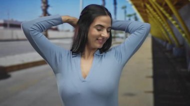 Genç İspanyol kadın esniyor ve açık havada güneşli bir sokakta uyuyor, mavi bir gömlek giyiyor, palmiye ağaçlarının altında ve açık mavi gökyüzünün keyfini çıkarıyor..