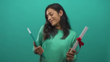 Stüdyoda elleri görünür ve eğimli bir şekilde diploma ve deniz mavisi kitabı tutarken gülümseyen kadın, mezuniyet gururu başarısı.