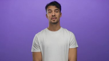 Beyaz tişört giyen İspanyol bir adam, izole edilmiş mor bir arkaplan üzerinde içten bir gülümsemeyle minnettarlık gösteriyor..