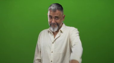 Yeşil stüdyoda el yapımı kalp jesti ile kamerayı işaret eden adam; dostça bir sıcaklık bağlantısı.