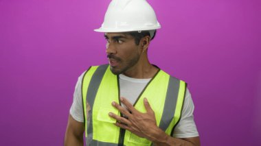 Beyaz kasketli ve yansıtıcı yelek giyen İspanyol mühendis stüdyoda göğsüne dokunuyor..