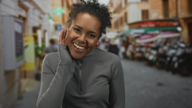 Kulak kabartan kadın, park etmiş scooterlar ve kafelerle dolu kalabalık bir caddede dikkatle dinliyor..