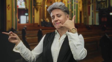 Beyaz gömlekli ve siyah yelekli kadın kilise binasının içinde süslü cam pencereleri ve ahşap sıraları olan bir parmak işaret ediyor..