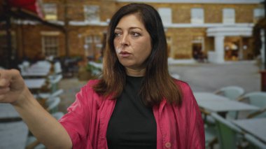 Kadın, restoranın terasını ciddi bir ifadeyle işaret ediyor ve kolunu uzatıyor. Acil uyarı..