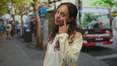 Kadın otobüs ve ağaçların yanında, çizgili tişört ve beyaz tişört giyen, kentin kendine güveni olan birini işaret ediyor..