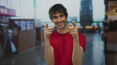 Havaalanı terminalindeki yoğun kalkış salonunda gülümseyen ve silah doğrultan kırmızı gömlekli adam..