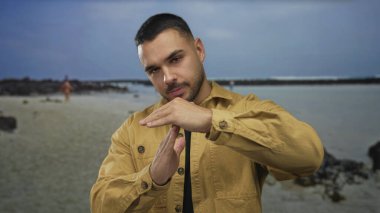 Kumlu sahilde sakin su kenarında iki avucunun önünde duran bir adam, durgunluğu durdurur..