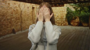 Dışarıdaki taş duvarlı arka planda gülümseyen genç kadın, doğal ışıkta mutluluğu ve günlük tarzını ifade ediyor, yaklaşılabilir sıcaklığı ve neşeli ambiyansı sergiliyor..