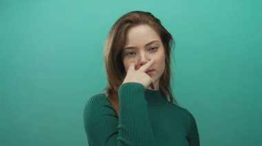 Yeşil kazaklı genç beyaz kadın önce göz göze gelir sonra bir stüdyo ortamında izleyiciye bakar..