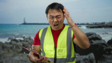 Güvenlik yeleği giyen bir adam deniz kenarındaki bir yerde hayal kırıklığına uğramış görünüyor. Okyanus geçmişi iş sorunları ya da iletişim sorunları olduğunu gösteriyor..