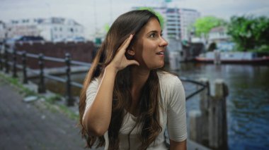 Amsterdam 'da bir caddede el ele tutuşan bir kadın, kanal seslerini dinlerken ağzı açık; merak keşfi.