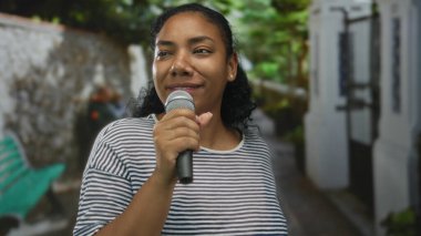 Afrikalı Amerikalı bir kadın mikrofon tutuyor dudaklarının kenarında gülümsüyor ve altın güneş ışığı altında şarkı söylüyor..