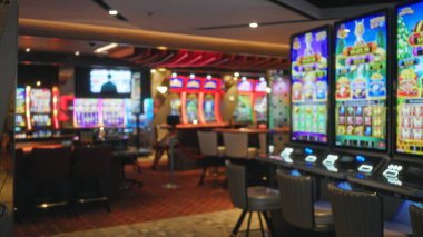 Kumar masası zemininde kumar makineleri, sandalyeler ve aydınlatılmış ekranlar hafifçe bulanık bokeh iç mekan; arka plan şablon örtüsü.