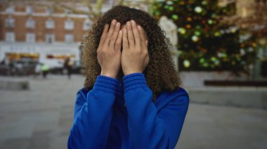 Kadın, bulanık noel ağacının ve bina cephesinin önündeki bir caddede iki eliyle tapınak tutuyor..