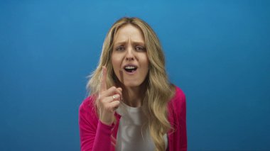 Duvarı işaret eden genç sarışın mavi arka planda cesur bir hareketle öfkesini vurguluyor..