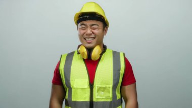 Sarı güvenlik yeleği ve kask giyen genç adam, izole edilmiş beyaz arka planda güvenle gülümsüyor ve profesyonel bir inşaat işçisini gösteriyor..