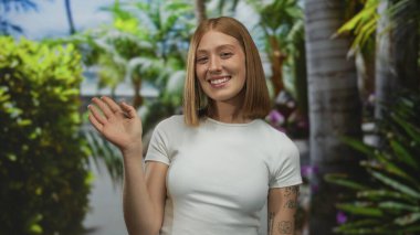 Güneşli bir parkta sallanan bir kadın, yemyeşil ve palmiye ağaçlarıyla çevrili, görünür dövmeleri olan, dostane bir gülümsemesi olan, sıradan ve samimi bir anı yakalayan..