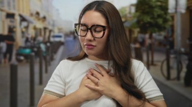 Kalabalık şehir caddesinde güneş ışığı altında gözlüklü genç İspanyol kadın sandık takıyor..