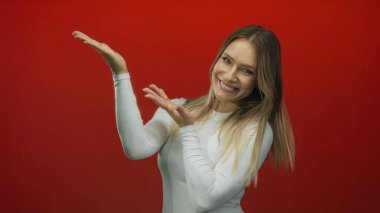 Beyaz bir jest içinde gülümseyen ve kollarını uzatan bir kadın, sağlam kırmızı bir arkaplan karşısında, tanıtım içeriği için dışavurumcu duygular ve dostça davranışlar sergiliyor..