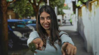 Genç İspanyol kadın her iki işaret parmağını caddede kameraya doğrulturken gülümsüyor; dostça bir davet.