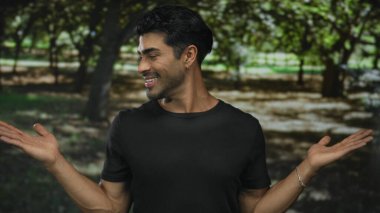 Adam uzun meşe ağaçları arasında açık yeşil orman parkında kollarını kaldırmış avuçlarını gösteriyor. Mutluluk..