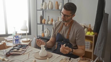 Stüdyoda el aletleriyle küçük bir seramik vazoyu zımparalayan bir adam, önlük ve gözlük takıyor; konsantrasyon sanatı sabrı.