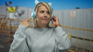 Kadın tek eliyle kedi kulaklığı ayarlıyor ve binanın yanında baş parmak işareti yapıyor. Onaylandı..