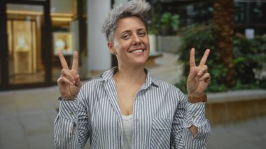Kadın, şehir caddesinde modern binanın önünde bir barış işareti jestinde iki elini de tutuyor..