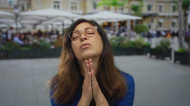 Avuç içli bir kadın, şehir binasının önündeki bir restoranın terasında dua jestinde birbirine bastırılmış..