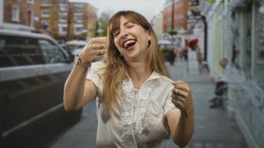 Meşgul bir şehir caddesinde avucunu kameraya doğru açan kadın gülümsüyor ve dur hareketi yapıyor; sevinç kutlaması.