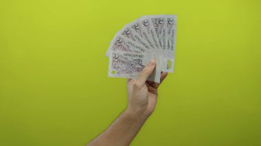 Singapur dolarlarını elinde tutan adam sarı arka plandaki gösterişli ekonomi ve finans kavramlarına izole edilmiş..