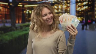 Sokakta gülümserken elinde banknotlar tutan kadın, para kentsel canlılık uyandırırken sarışın genç cazibesini ön plana çıkarıyor..