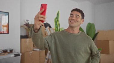 Yeni binada çağrı sırasında gülümserken kırmızı akıllı telefonu tutan adam el sallıyor; sanal bağlantı.