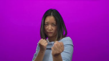 Genç bir kadın güçlü olduğunu ve odaklandığını ifade eden canlı pembe bir arka plana karşı yumruğunu sıkarak azim gösteriyor..