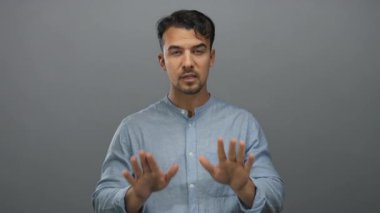 Mavi tişörtlü genç İspanyol adam. Gri arka plana karşı sinirli bir ifadeyle hayır diyor. Olumsuz duygular ve reddedişler aktarıyor..