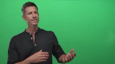 Elleri açık ve kolları açık bir adam, avuçları yeşil stüdyoda hafif bir gülümseme ile yukarda; davet güven karşılama.