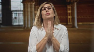 Beyaz gömlek giyen ve elleri bağlı gözlüklü bir kadın geceleri aydınlık atari sütunlarının altında sokakta dua ederken; umut.