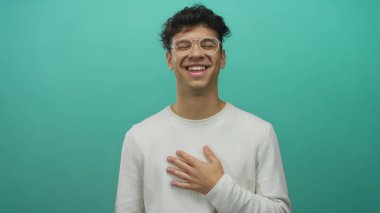 Stüdyo ortamında eli göğsünde gözlük takan İspanyol genç adam gülüyor..