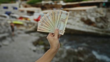 Deniz kenarındaki bulanık plaj geçmişiyle elinde kara para tutan bir adam açık hava ortamında finansal işlem kavramını resmediyor..