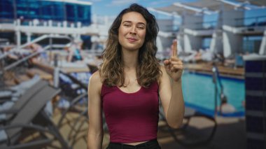 Kadın, güneşli ortamda havuz ve oturma odalarıyla güvertedeki objeyi işaret ediyor; kendine güven.