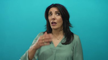 İspanyol orta yaşlı, yeşil bluz ve inci kolye giyen bir kadın gözlerini kapatır ve kafasını turkuaz stüdyo duvarına yaslar; dinginlik iç gözlem meditasyonu.