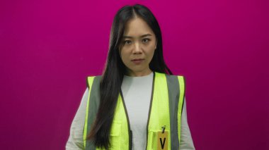 Yansıtıcı yelek giymiş bir kadın, her iki orta parmağıyla canlı pembe bir duvara karşı hareketler yapıyor. Cesur bir yüz ifadesiyle meydan okuyor ve gönüllü üniformasının altını çiziyor..