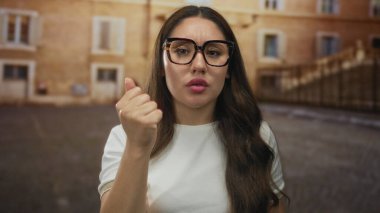 Eski şehir caddesinde tarihi binanın önünde ciddi ifade yeteneği olan bir kadın yumruğunu sıkar; iç yansıması.