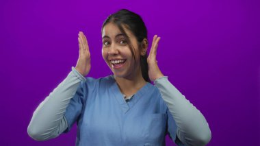 İspanyol kadın kafasını mor stüdyoda elleriyle çerçeveler ve gülümser, yüzünün etrafında bir insan çerçevesi oluşturur; oyuncu yaratıcılık.