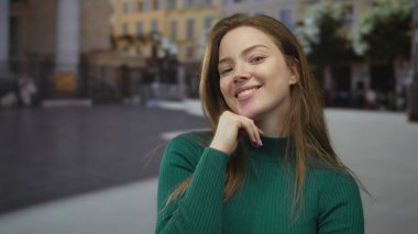 Gündüz vakti güneşli şehir caddesinde yeşil kazaklı bir kadın çenesinde dinleniyor. Düşünceli bir düşünce..