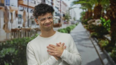 Şehir sokağında palmiye ağaçlarıyla kaplı beyaz kazak giyen adam kalp krizi geçiriyor..